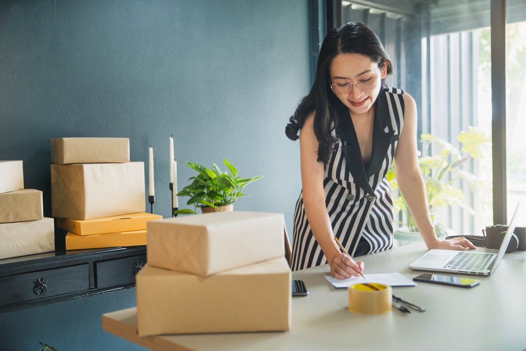 Asian woman working at her desk with boxes in front of her.